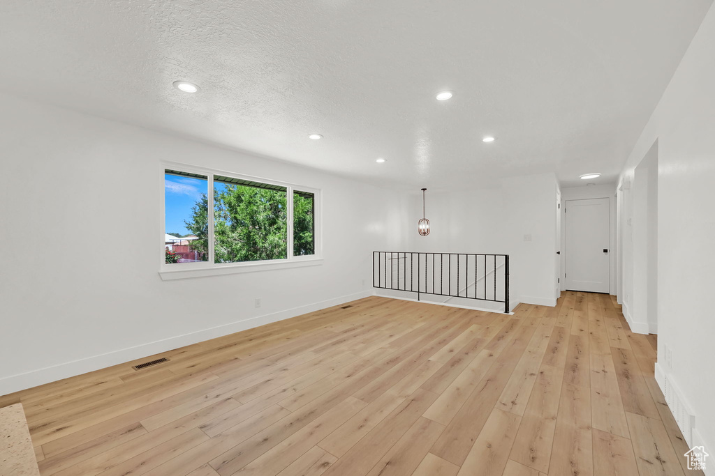 Empty room featuring recessed lighting, baseboards, light wood-type flooring, and a textured ceiling