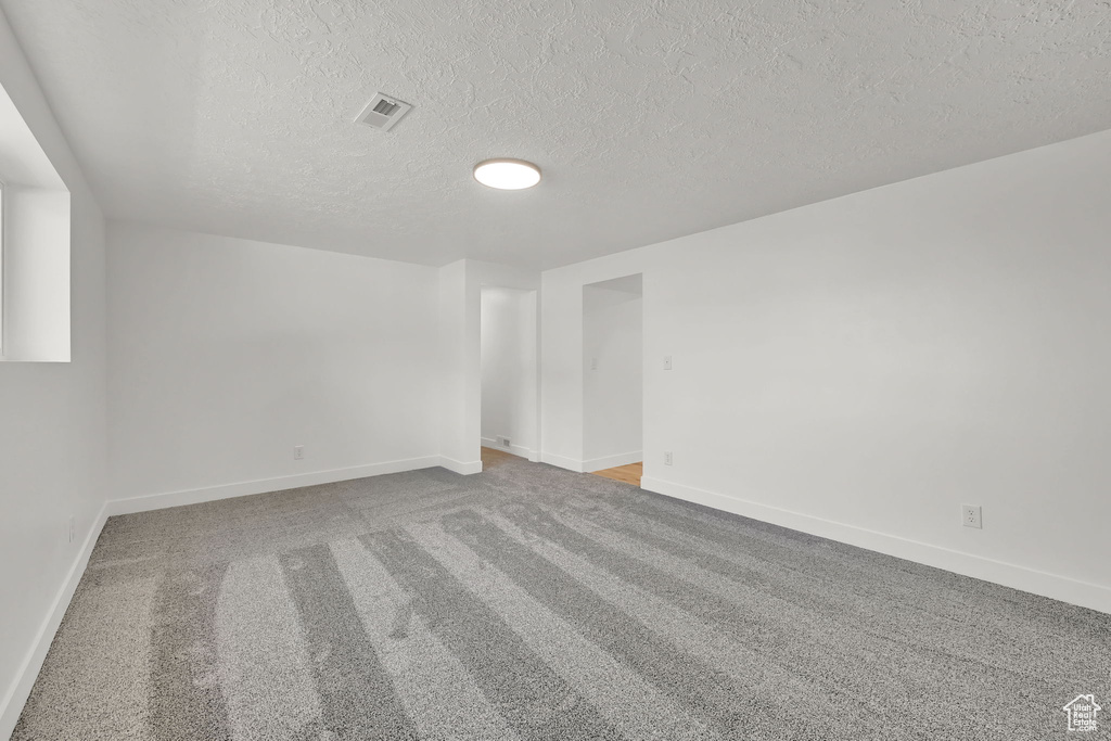 Carpeted spare room featuring a textured ceiling and baseboards