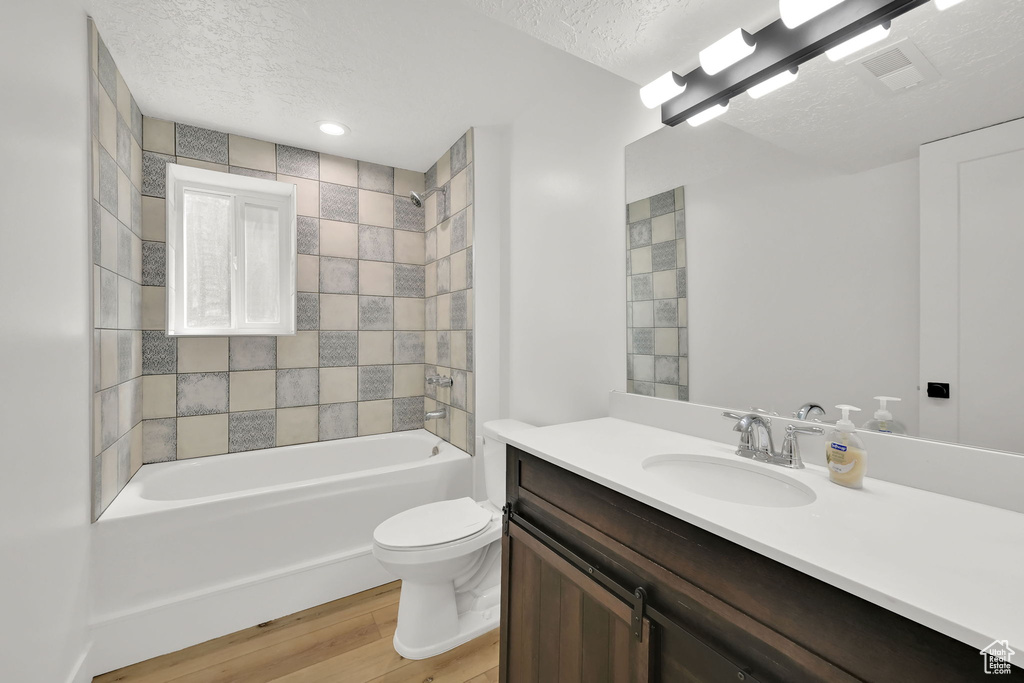 Full bathroom with a textured ceiling, vanity, toilet, shower / tub combination, and wood finished floors