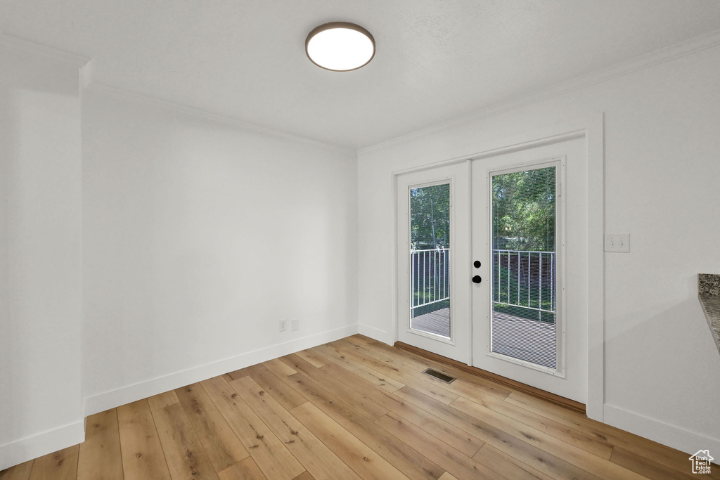 Spare room featuring french doors, ornamental molding, light wood-style floors, and baseboards