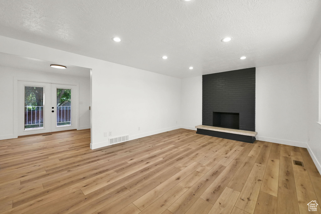 Unfurnished living room with light wood-type flooring, a textured ceiling, french doors, recessed lighting, and a fireplace