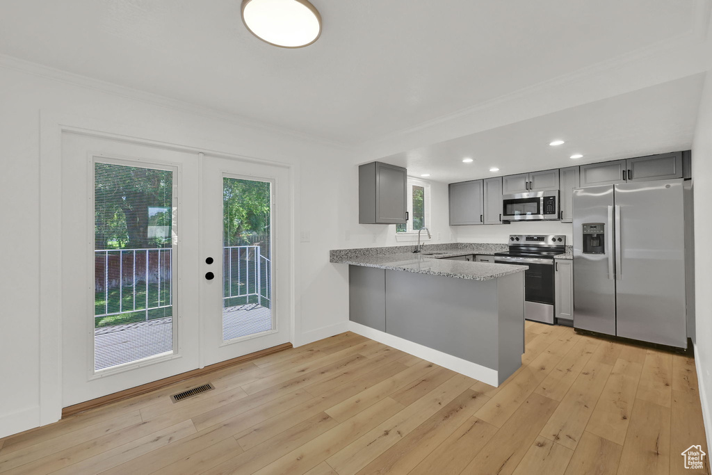 Kitchen with appliances with stainless steel finishes, gray cabinets, french doors, a peninsula, and light wood-style floors