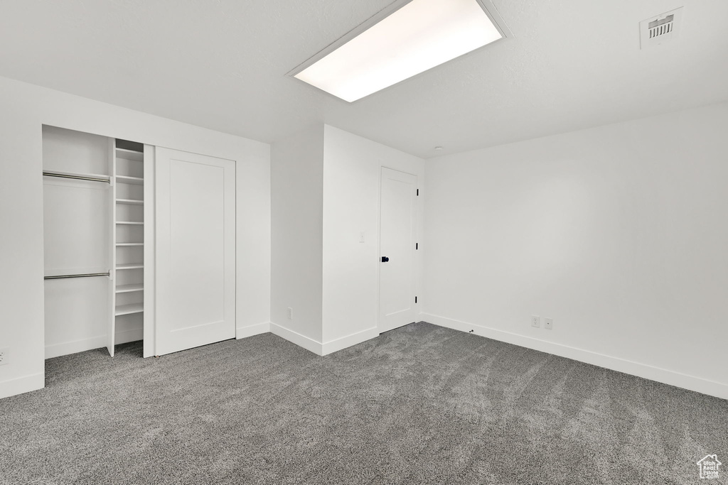 Unfurnished bedroom featuring dark colored carpet, baseboards, and a closet