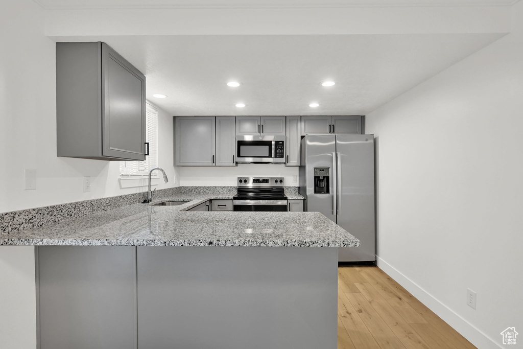 Kitchen with appliances with stainless steel finishes, gray cabinets, a sink, light stone countertops, and recessed lighting