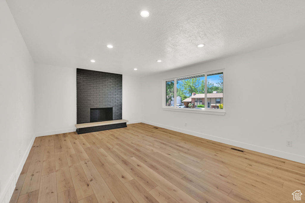 Unfurnished living room with a brick fireplace, recessed lighting, light wood-type flooring, baseboards, and a textured ceiling