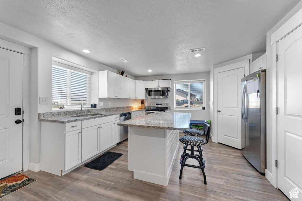 Kitchen with appliances with stainless steel finishes, a sink, a textured ceiling, a kitchen bar, and light wood-type flooring