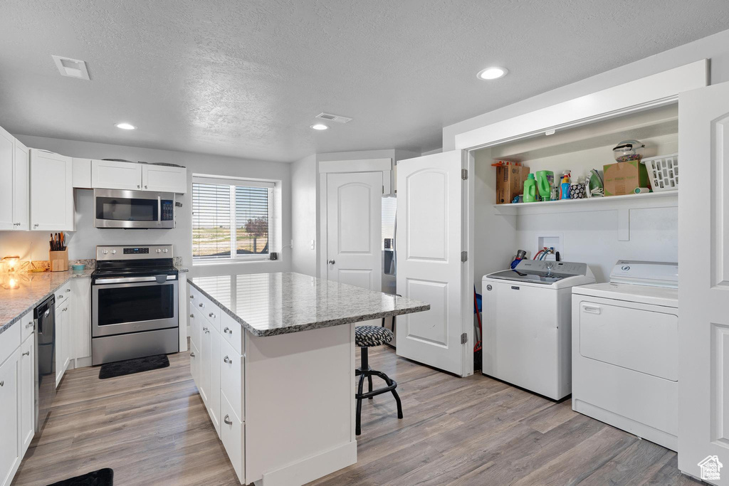 Kitchen with appliances with stainless steel finishes, washing machine and dryer, white cabinets, a textured ceiling, and light wood-style flooring