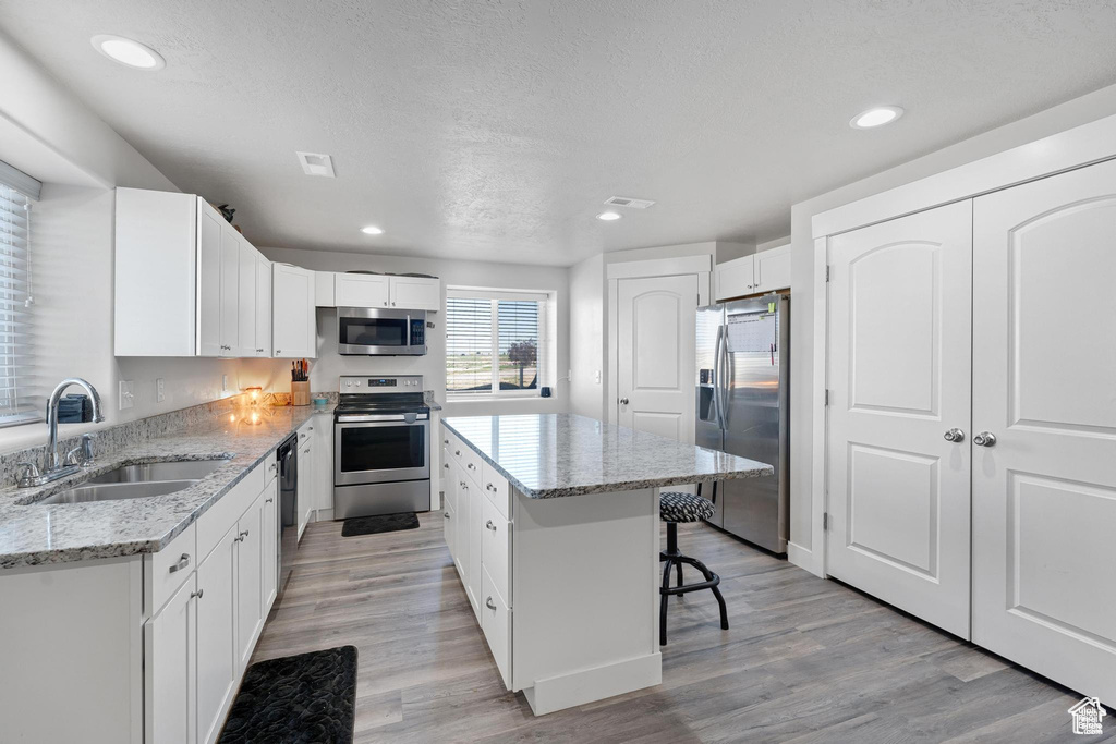 Kitchen with stainless steel appliances, a sink, light wood-style flooring, a center island, and a breakfast bar area