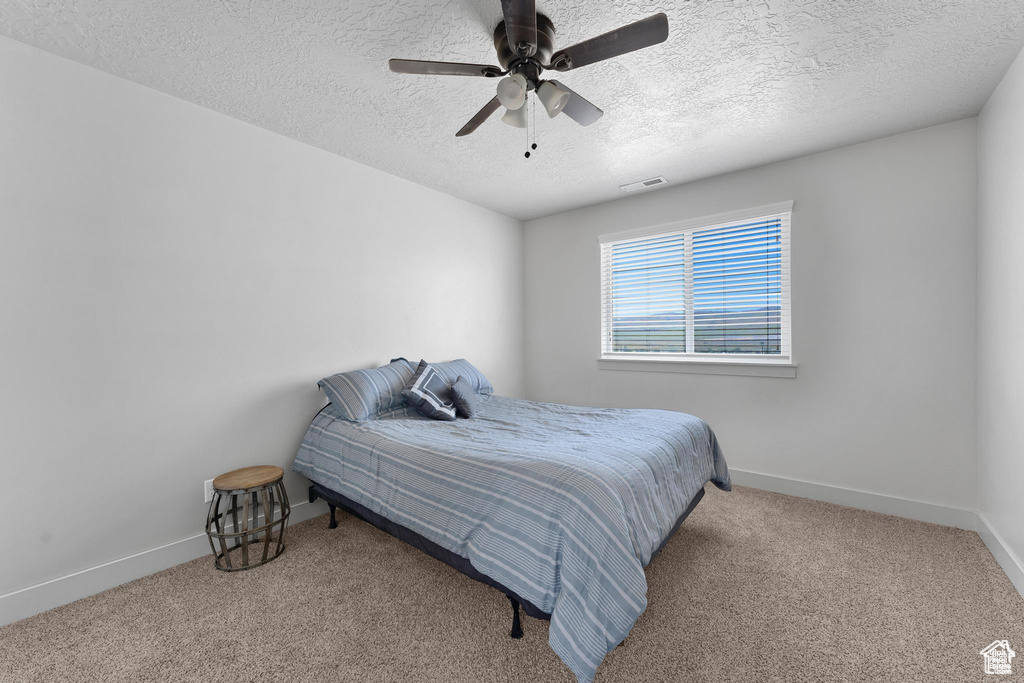 Bedroom featuring a textured ceiling, carpet flooring, baseboards, and a ceiling fan