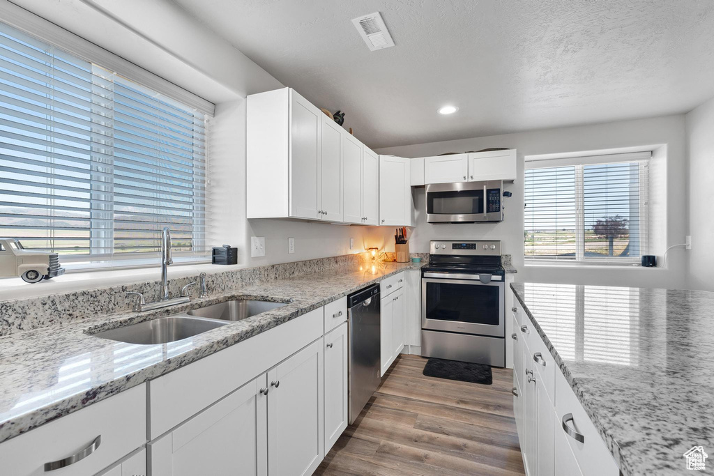 Kitchen featuring stainless steel appliances, a sink, recessed lighting, wood finished floors, and white cabinets
