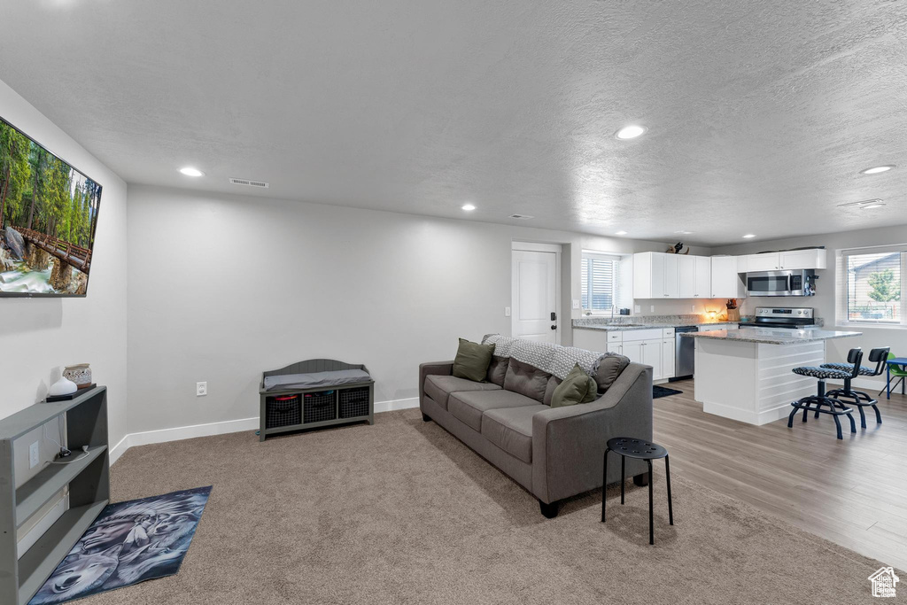 Living room with recessed lighting, baseboards, a textured ceiling, and light wood-style flooring