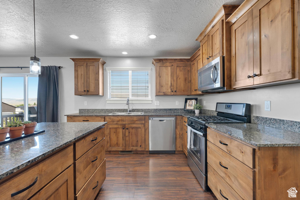 Kitchen featuring stainless steel appliances, a sink, brown cabinets, dark wood-type flooring, and a textured ceiling