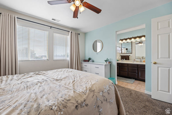 Bedroom with light carpet, ensuite bath, and a ceiling fan