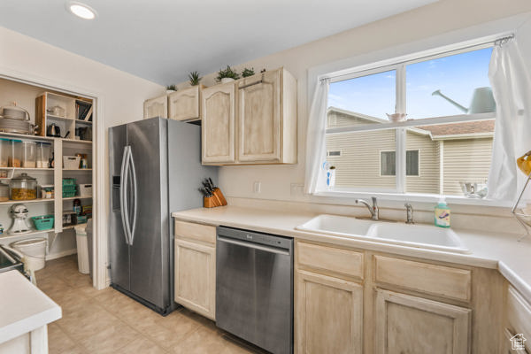 Kitchen featuring appliances with stainless steel finishes, light brown cabinets, a sink, and light countertops