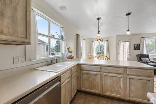 Kitchen with stainless steel dishwasher, a sink, a peninsula, light brown cabinets, and light countertops