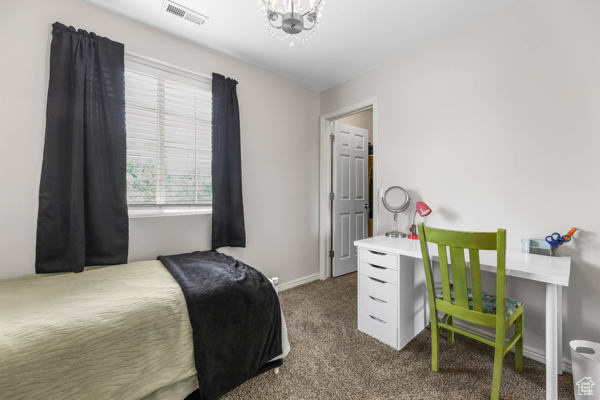 Bedroom with dark colored carpet, a chandelier, and baseboards