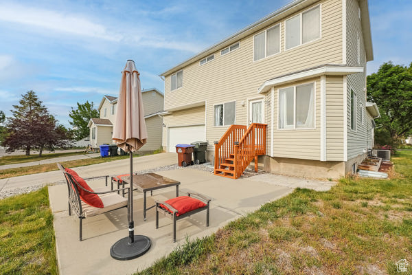 Rear view of property with central AC, an attached garage, and a lawn