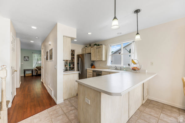Kitchen with appliances with stainless steel finishes, light countertops, a peninsula, light brown cabinetry, and hanging light fixtures
