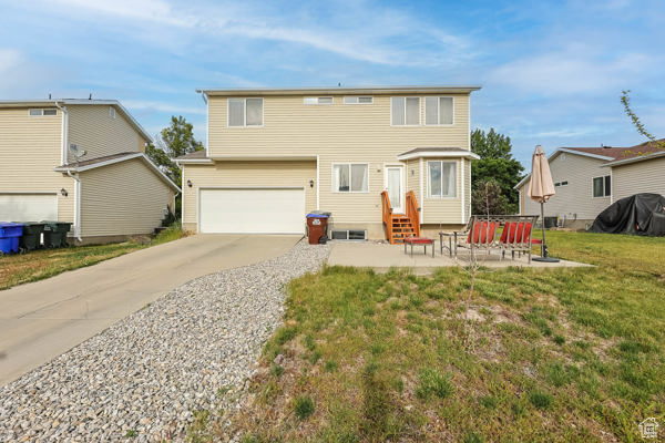 Rear view of property featuring entry steps, a garage, driveway, and a yard
