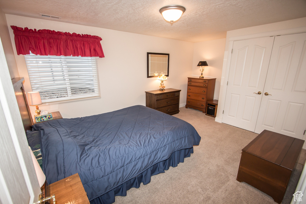 Bedroom with a textured ceiling, light colored carpet, and a closet