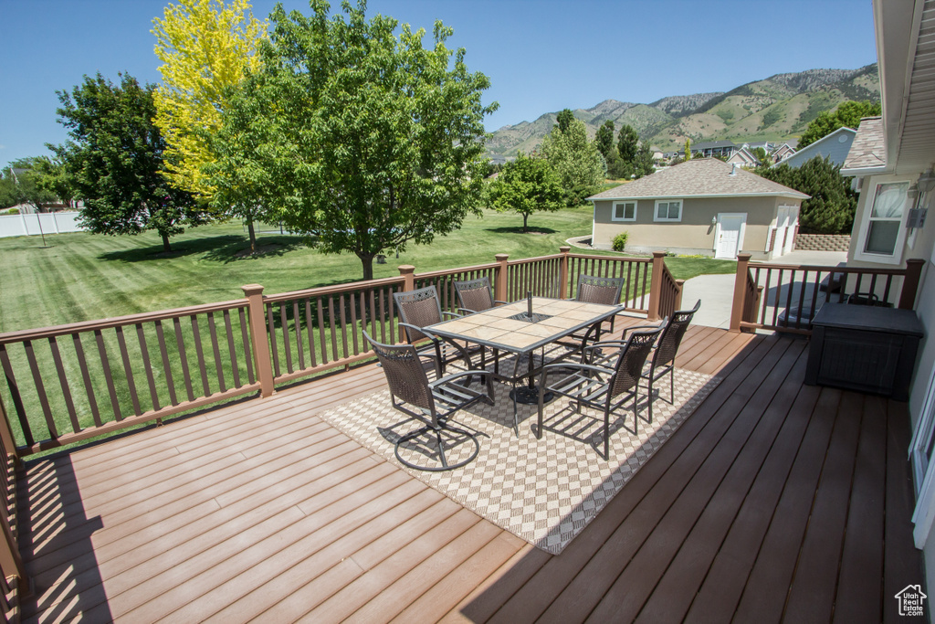 Deck with outdoor dining space, a lawn, and a mountain view