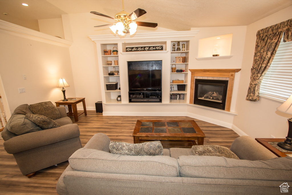 Living room with a glass covered fireplace, wood finished floors, a ceiling fan, baseboards, and built in features