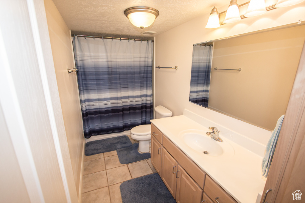 Bathroom featuring vanity, toilet, tile patterned flooring, a textured ceiling, and curtained shower