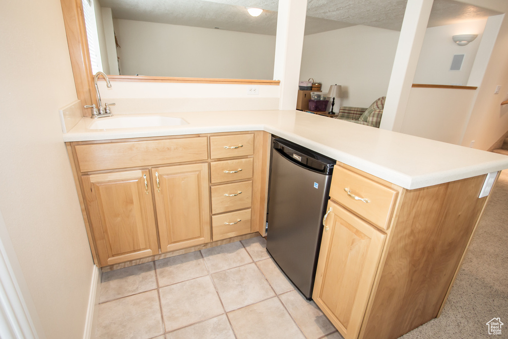 Kitchen with light brown cabinets, a sink, dishwashing machine, and light countertops
