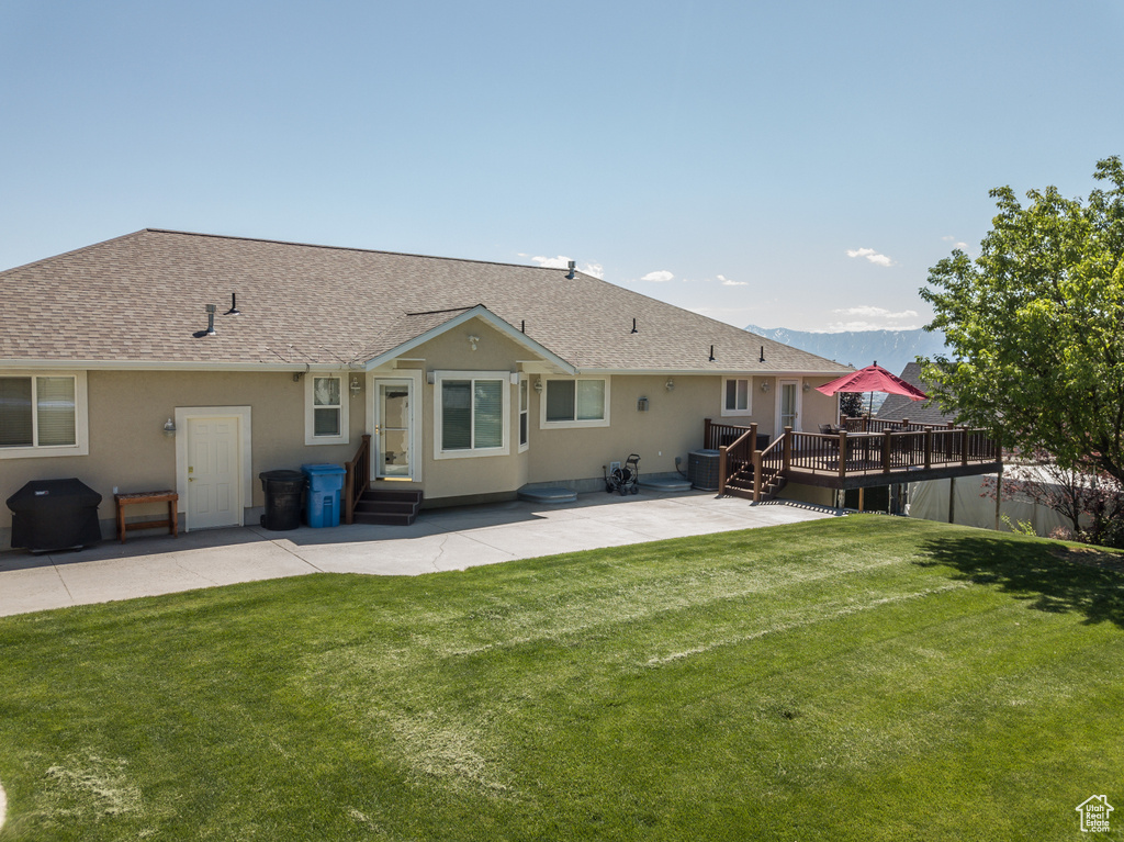 Back of house featuring a patio area, a deck, a shingled roof, a lawn, and stucco siding