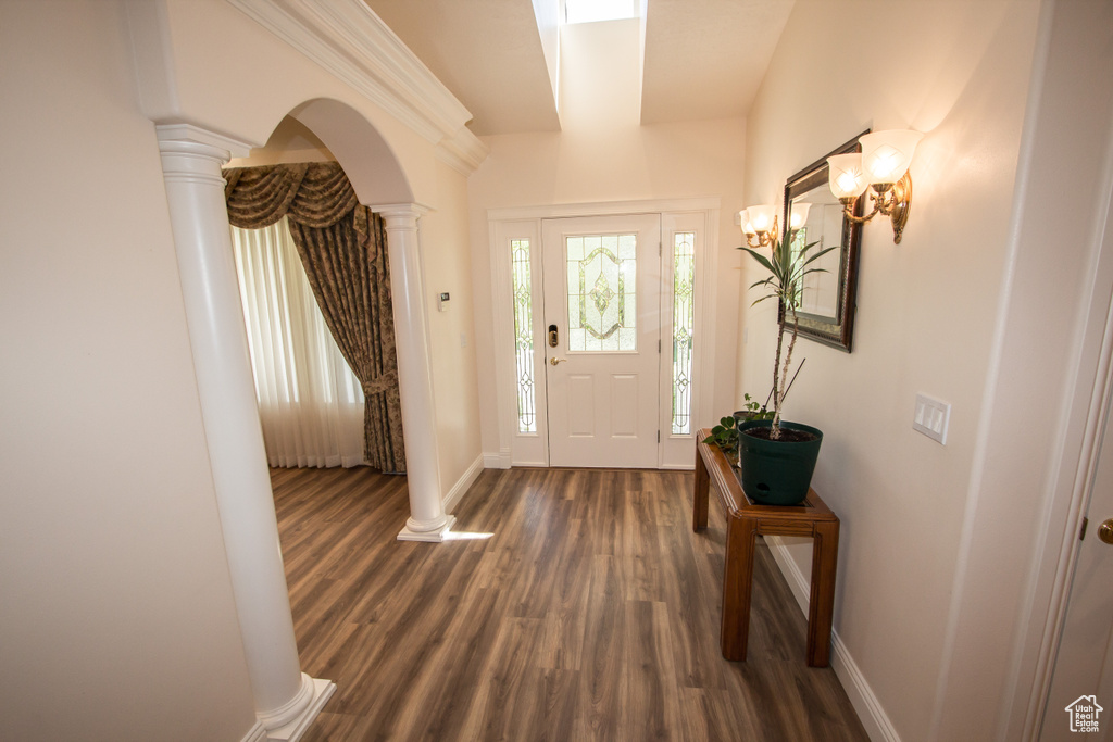 Foyer entrance with decorative columns, dark wood-style floors, baseboards, and arched walkways
