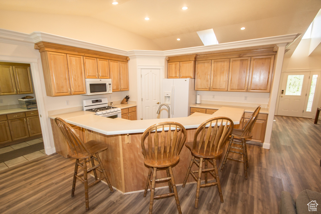 Kitchen featuring white appliances, vaulted ceiling, a sink, dark wood finished floors, and a breakfast bar
