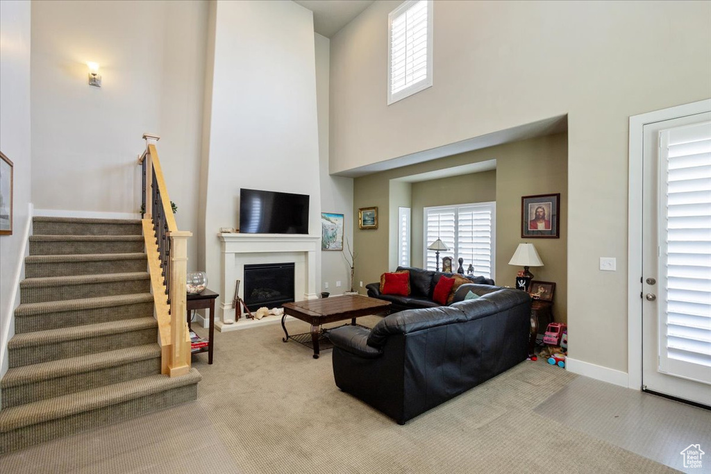 Carpeted living area featuring stairway, a fireplace, a high ceiling, and baseboards