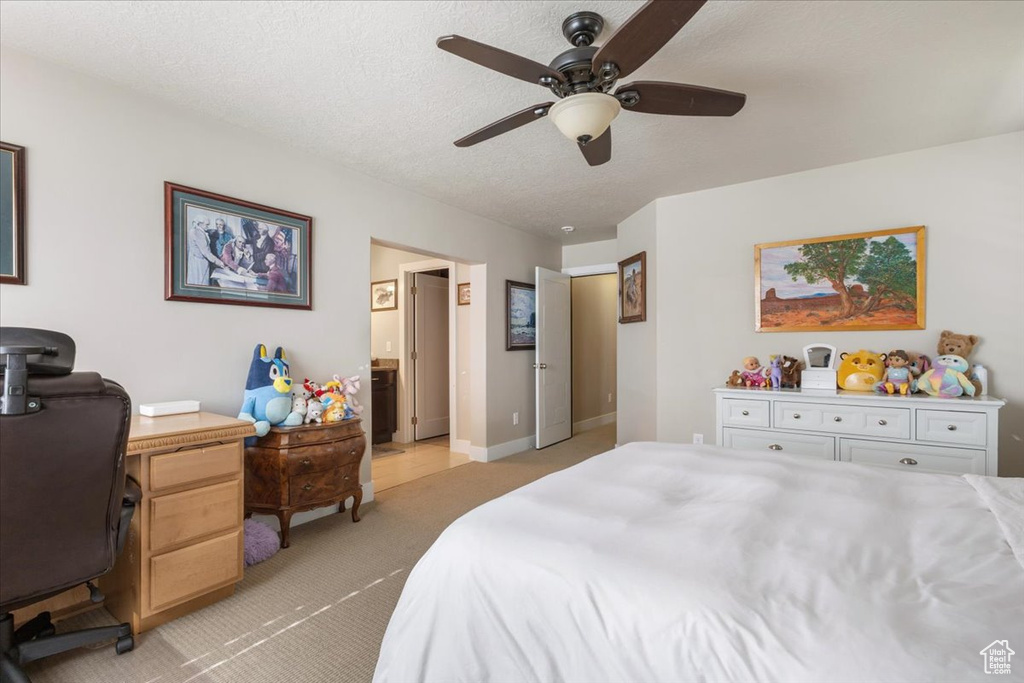 Bedroom with light carpet, an office area, a textured ceiling, ceiling fan, and ensuite bath