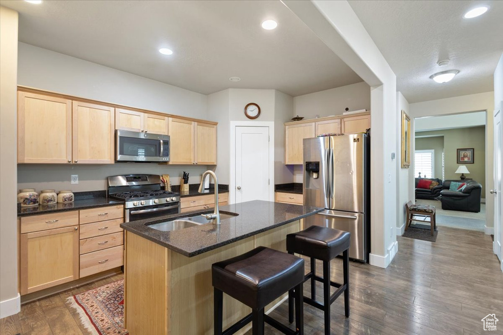 Kitchen featuring appliances with stainless steel finishes, light brown cabinetry, a sink, a breakfast bar area, and dark wood-style flooring