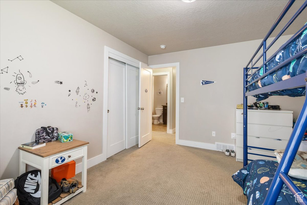 Carpeted bedroom with a textured ceiling, baseboards, and a closet