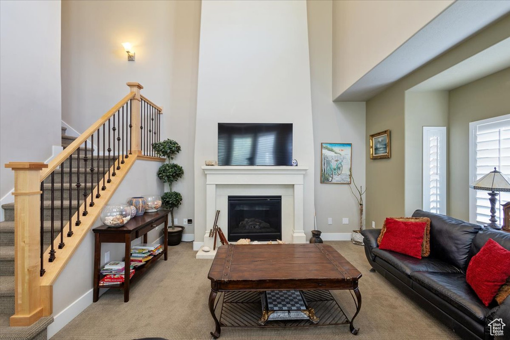 Living room with carpet, a glass covered fireplace, stairway, baseboards, and a towering ceiling