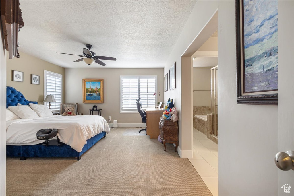 Bedroom with light carpet, baseboards, a textured ceiling, ensuite bath, and ceiling fan