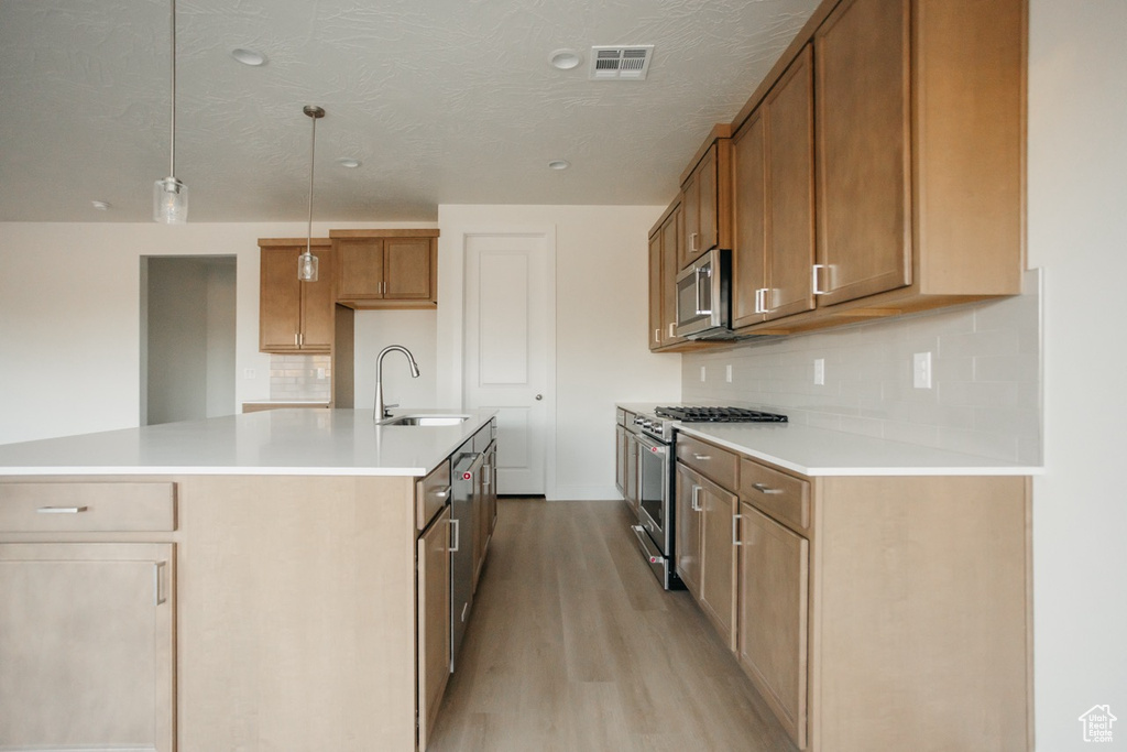 Kitchen with appliances with stainless steel finishes, a sink, light wood-style flooring, decorative backsplash, and brown cabinetry