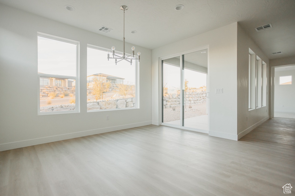 Unfurnished room featuring light wood finished floors, baseboards, and a chandelier