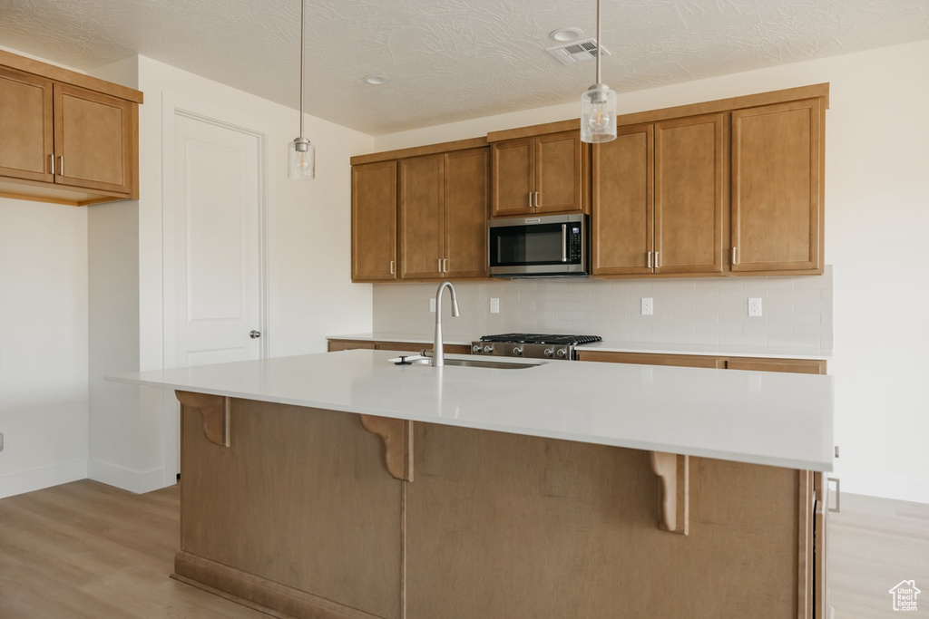 Kitchen with stainless steel microwave, light wood-style flooring, brown cabinetry, a sink, and tasteful backsplash