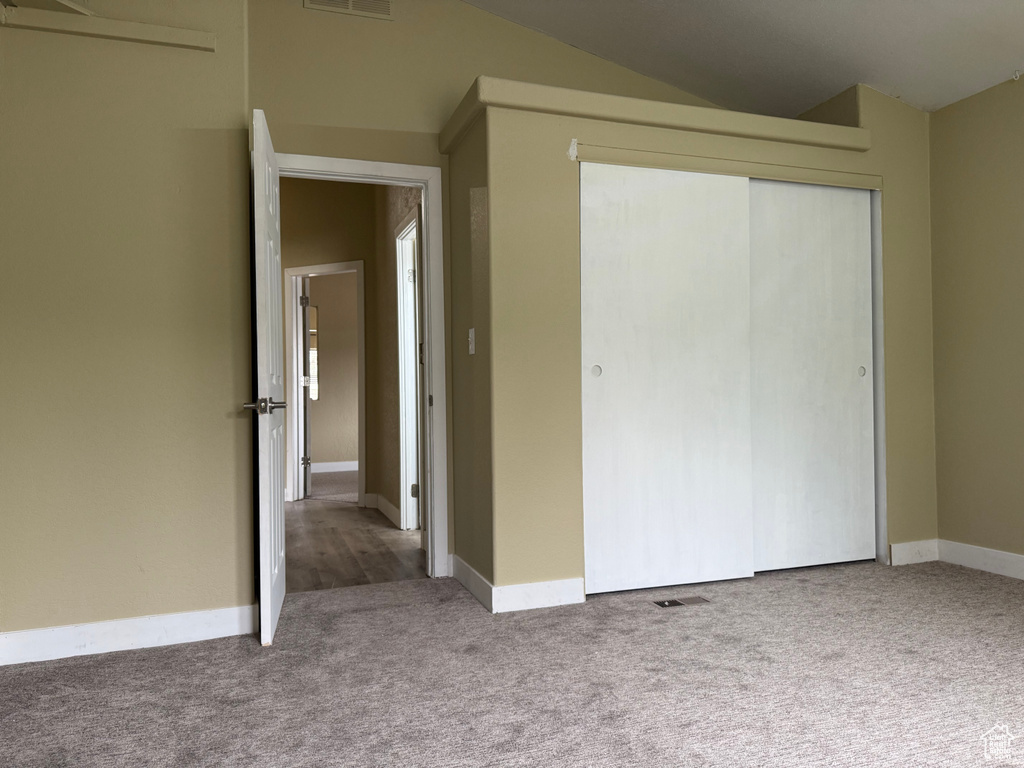 Unfurnished bedroom featuring carpet floors, a closet, baseboards, and lofted ceiling