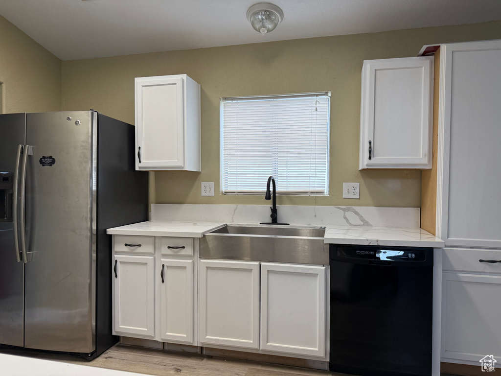 Kitchen featuring stainless steel refrigerator with ice dispenser, dishwasher, a sink, white cabinets, and light stone countertops
