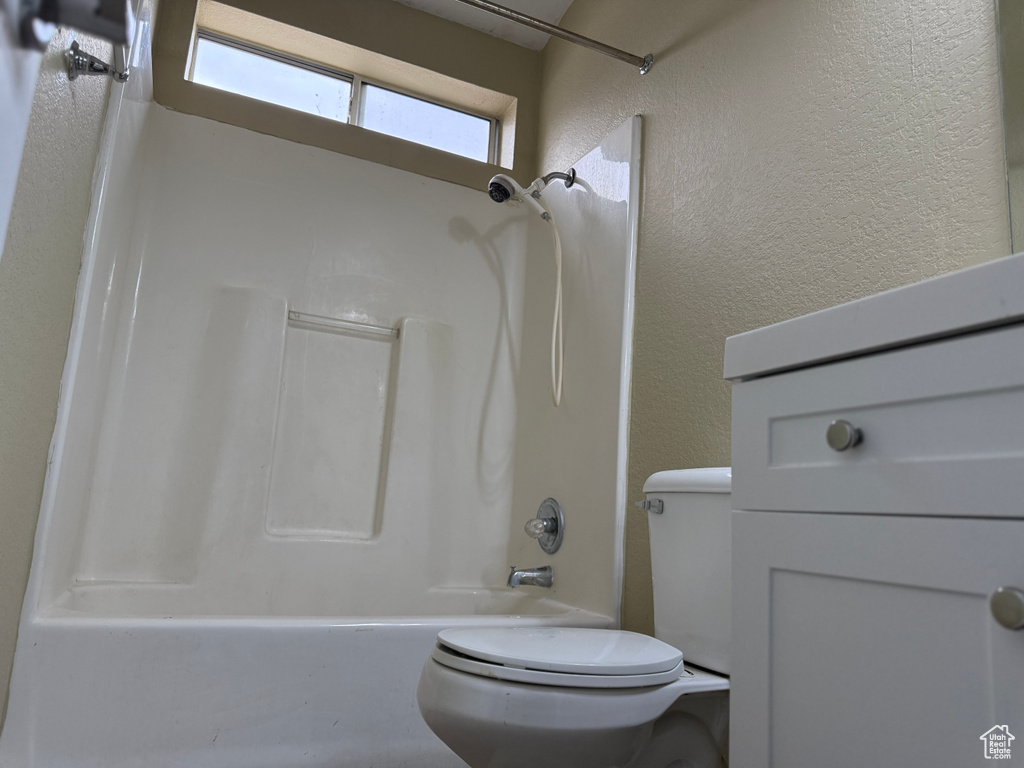 Full bath with toilet, a textured wall, and shower / tub combination