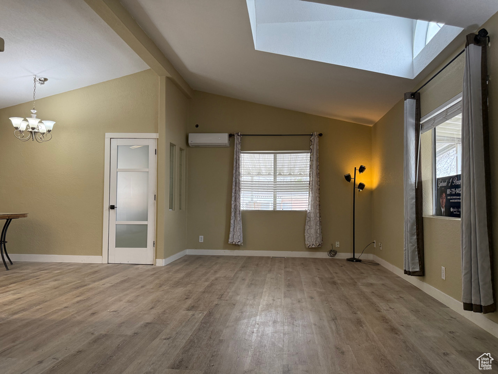 Unfurnished living room with lofted ceiling, a wall mounted air conditioner, wood finished floors, healthy amount of natural light, and a chandelier