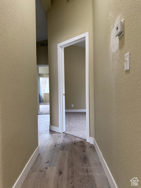 Hallway with a textured wall, wood finished floors, and baseboards