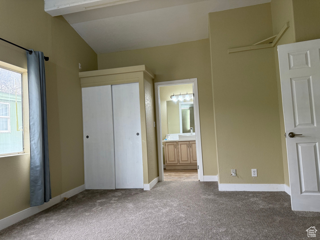 Unfurnished bedroom with carpet, a closet, lofted ceiling, ensuite bath, and baseboards