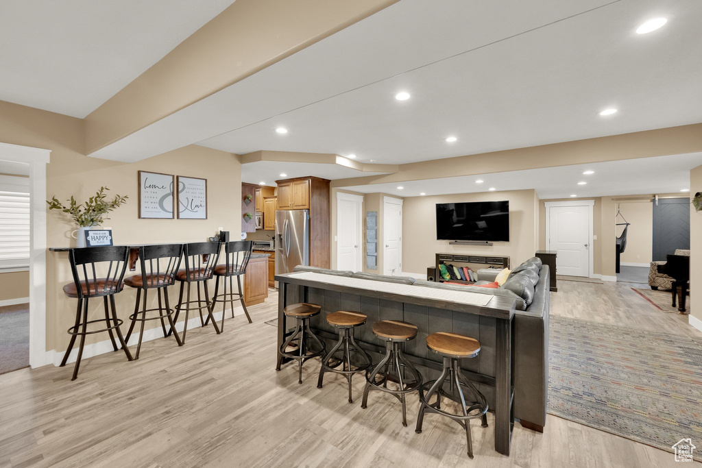 Kitchen featuring a breakfast bar, stainless steel fridge with ice dispenser, light wood finished floors, recessed lighting, and baseboards