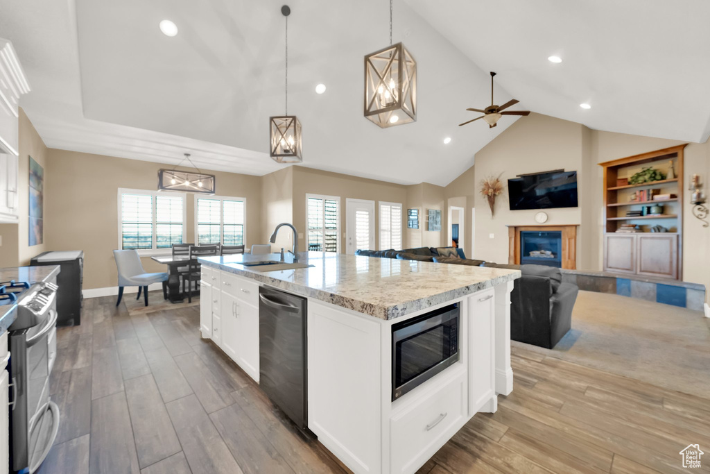 Kitchen with stainless steel appliances, a sink, wood finished floors, light stone countertops, and a kitchen island with sink
