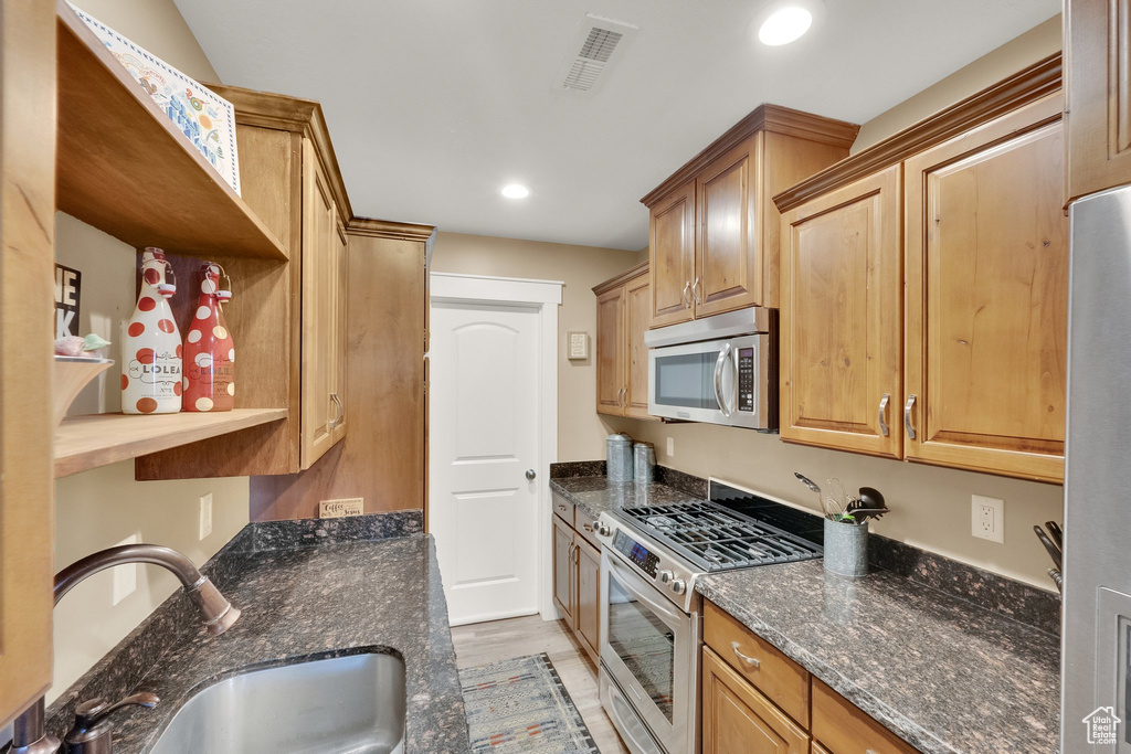 Kitchen featuring appliances with stainless steel finishes, a sink, dark stone countertops, recessed lighting, and light wood-style flooring
