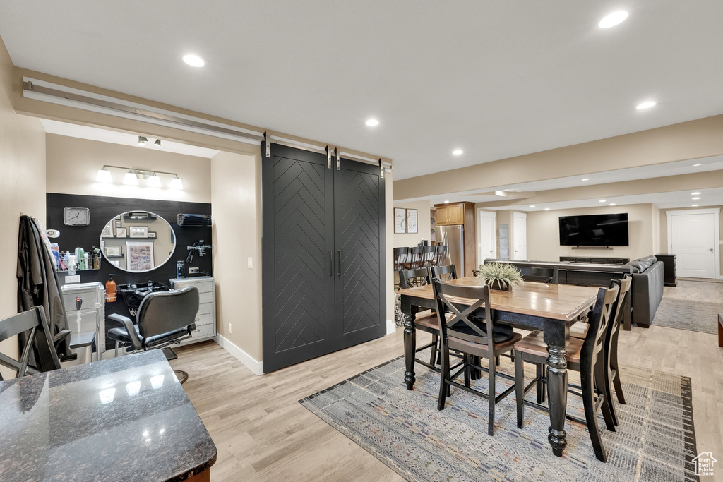 Dining space with a barn door, light wood-type flooring, recessed lighting, and baseboards